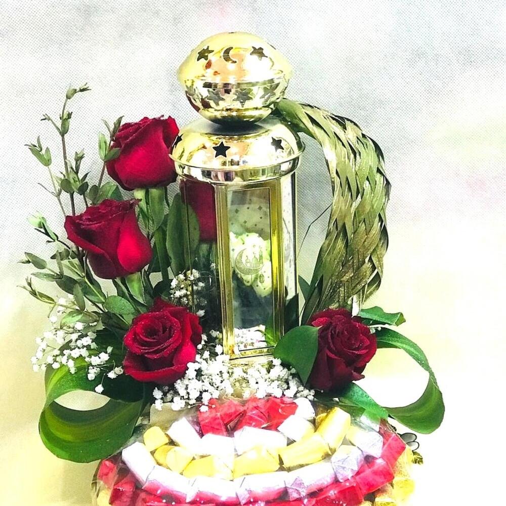 Golden lantern centerpiece with red roses, lush greenery, and colorful candies, perfect for festive occasions.