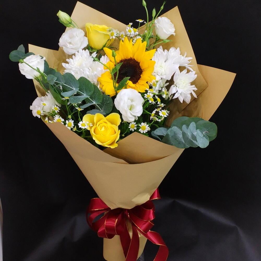 Bouquet of sunflowers, white roses, and daisies wrapped in brown paper with a red ribbon on a black background.