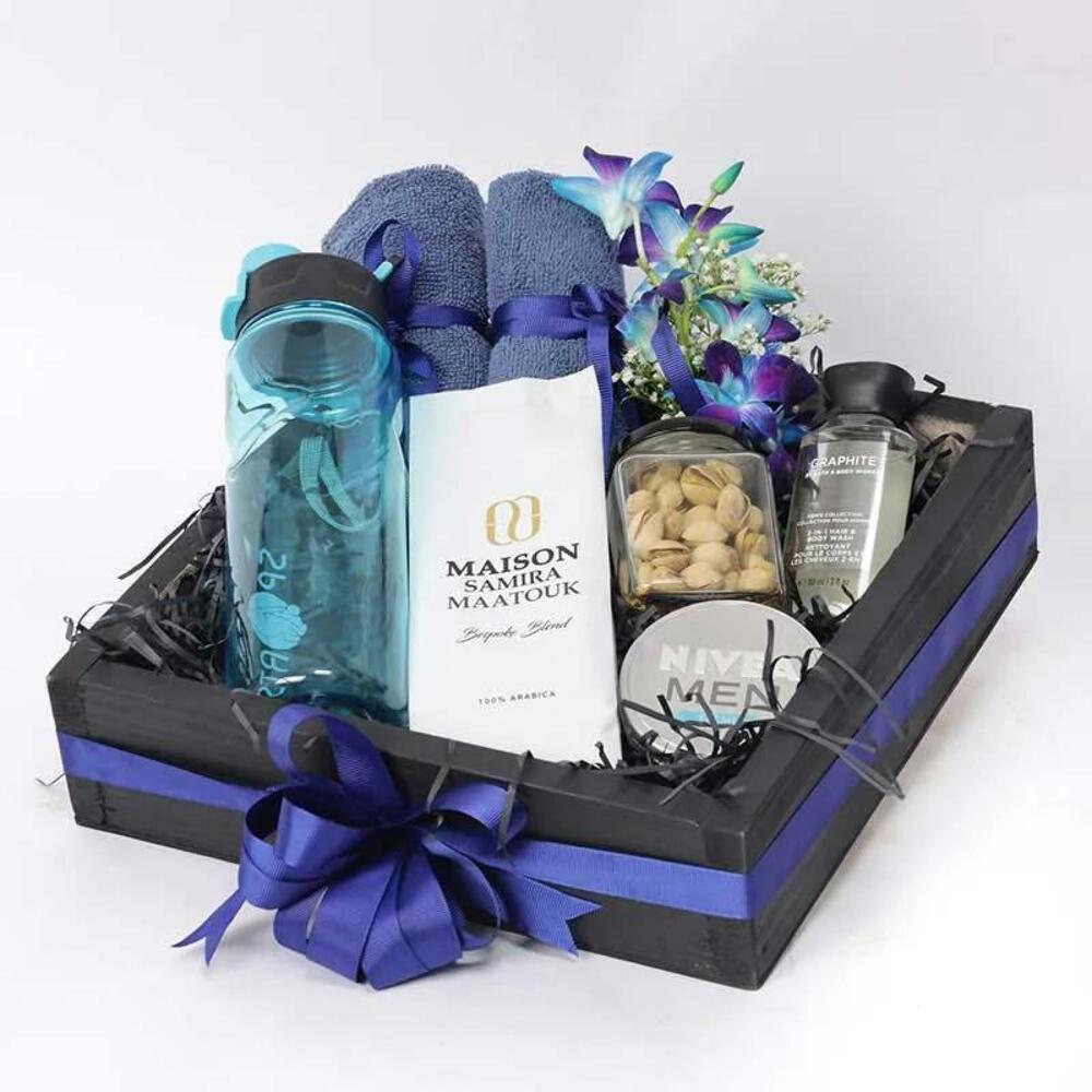 Gift basket with coffee, water bottle, towels, pistachios, lotion, and flowers, adorned with blue ribbon. Perfect for relaxation.