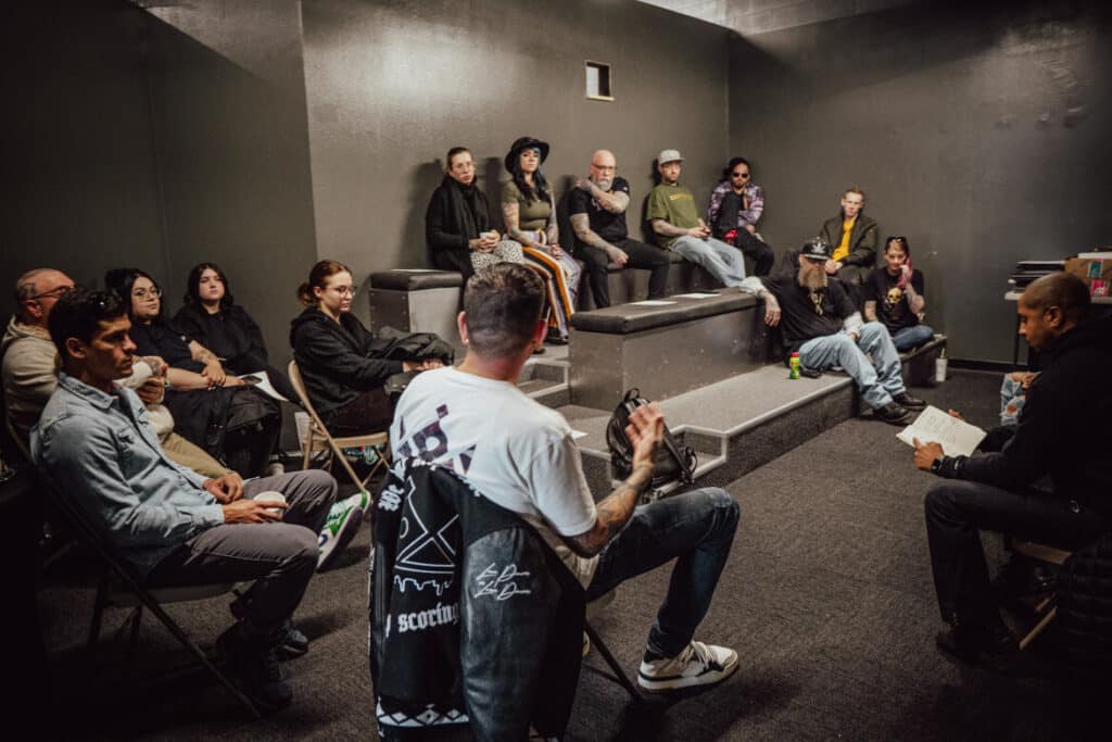 Group of people in a discussion meeting, seated in a dimly lit room, some taking notes.