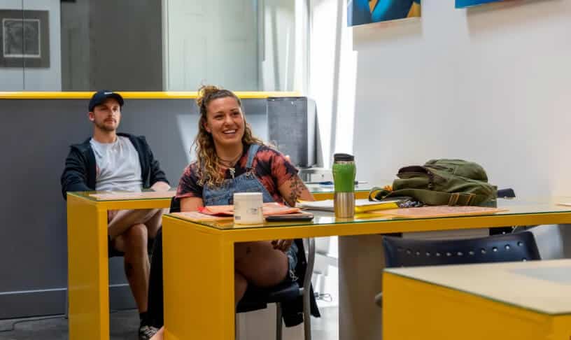 Two people sitting at yellow tables in a modern classroom, smiling and engaged.