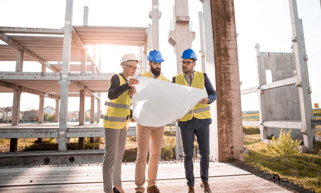 Engineers in safety gear review blueprints at a construction site, planning structural development.