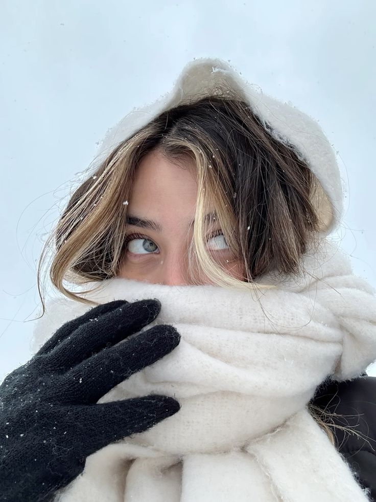 Person in a cozy winter scarf and gloves, gazing upward in snowy weather.