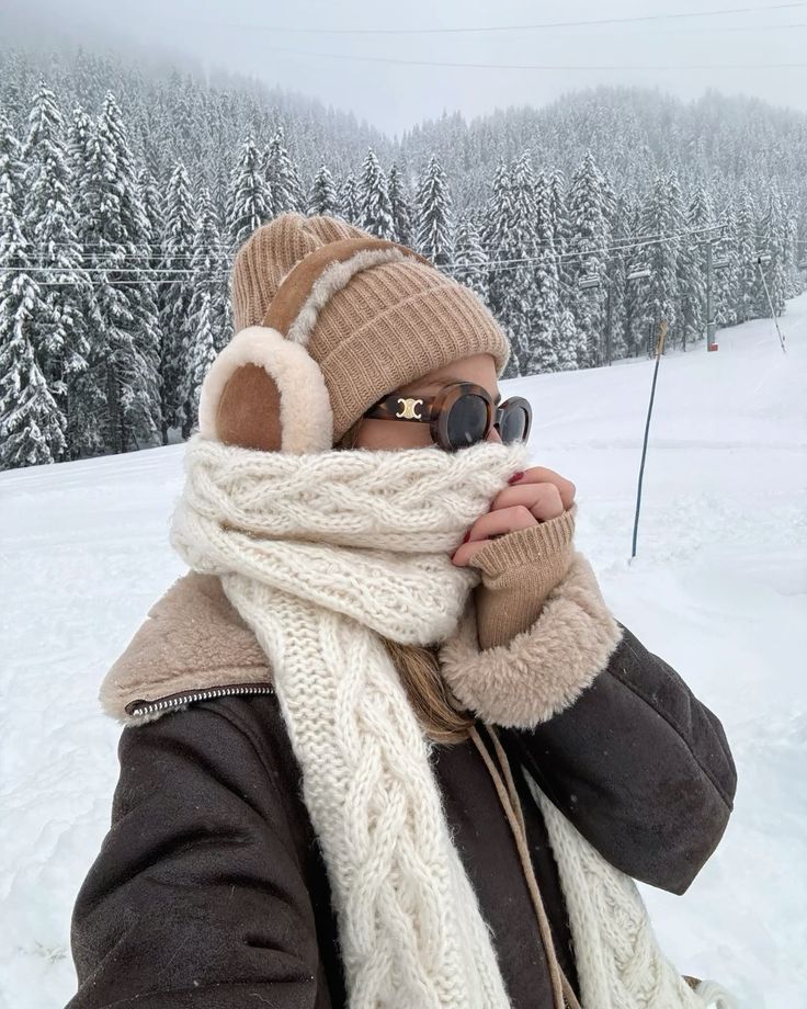 Person in winter clothes with scarf and earmuffs in snowy forest.