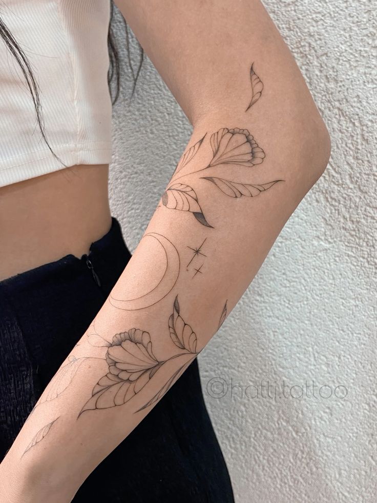 Minimalist floral and crescent moon tattoo on arm with delicate leaves and stars.