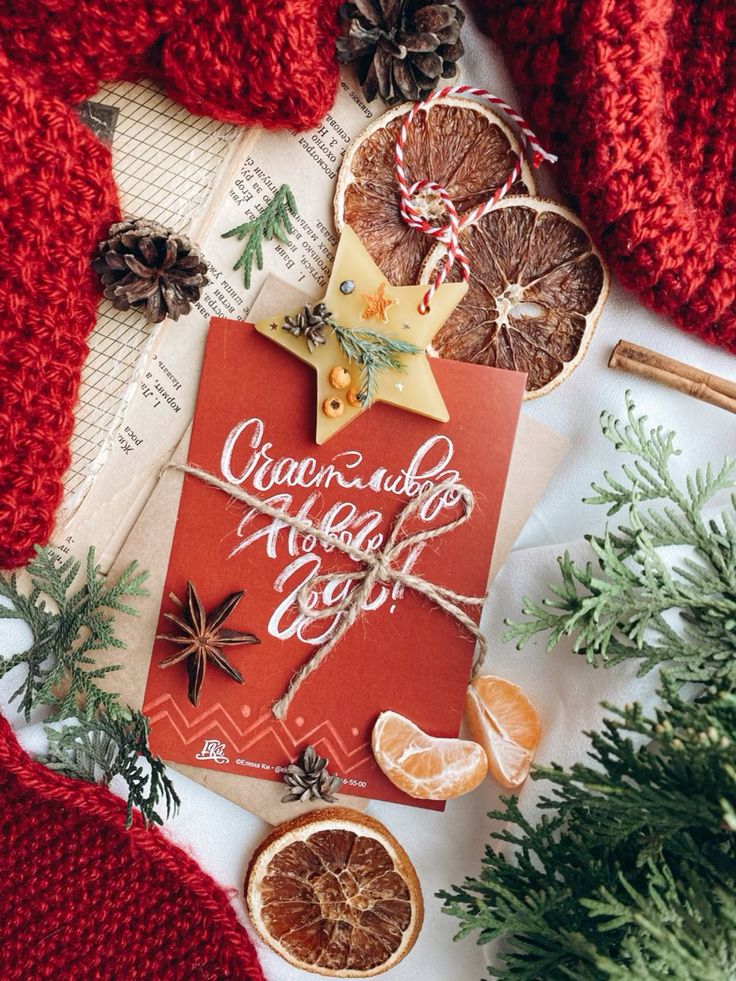 Festive flat lay with red card, dried oranges, pinecones, star anise, and spruce branches on cozy winter backdrop.