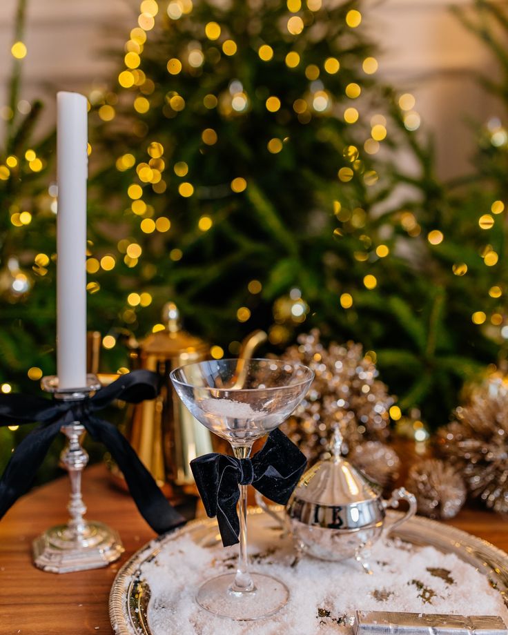 Festive holiday table setting with a martini glass, candle, and decorations in front of a sparkling Christmas tree.