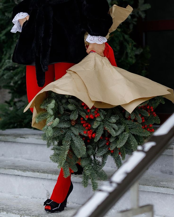 Person holding a festive Christmas wreath with red berries, wrapped in brown paper, on stone steps.