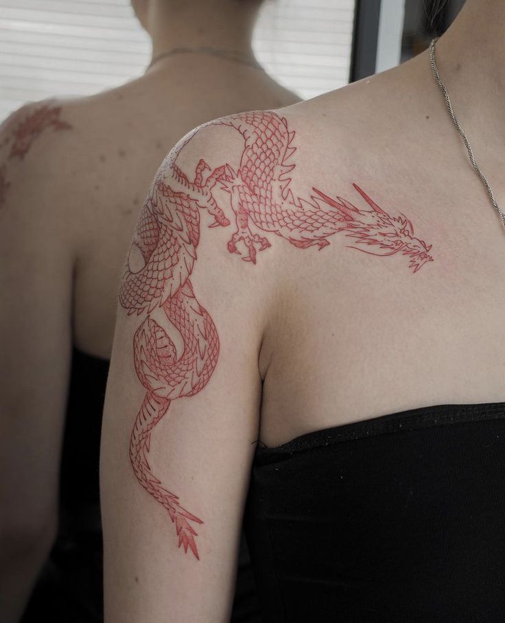 Red dragon tattoo on woman's shoulder, mirrored reflection, wearing black top.