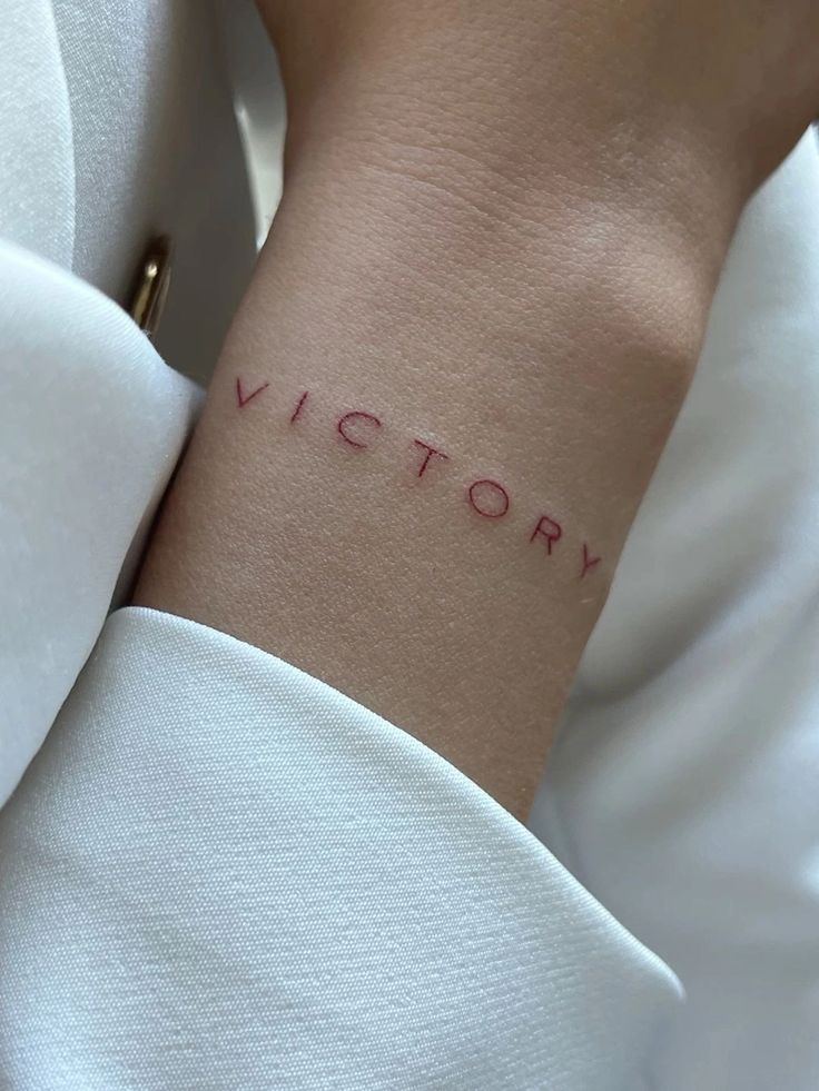 Minimalist Victory tattoo on wrist in red ink, close-up view.