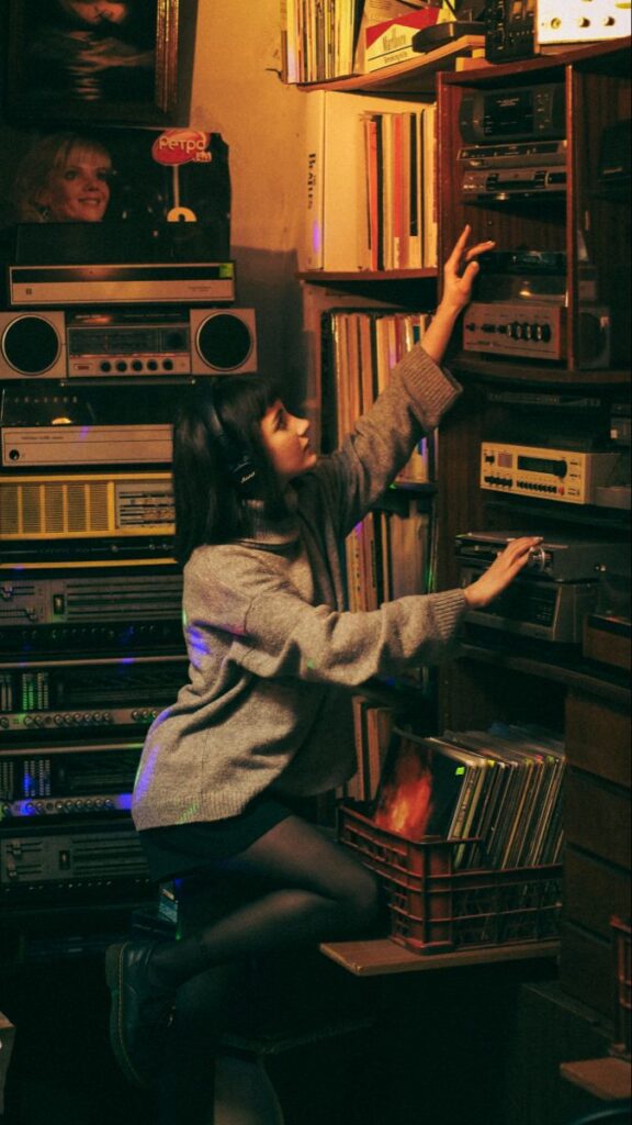 Young woman with headphones adjusting vintage stereo in cozy retro-themed room.