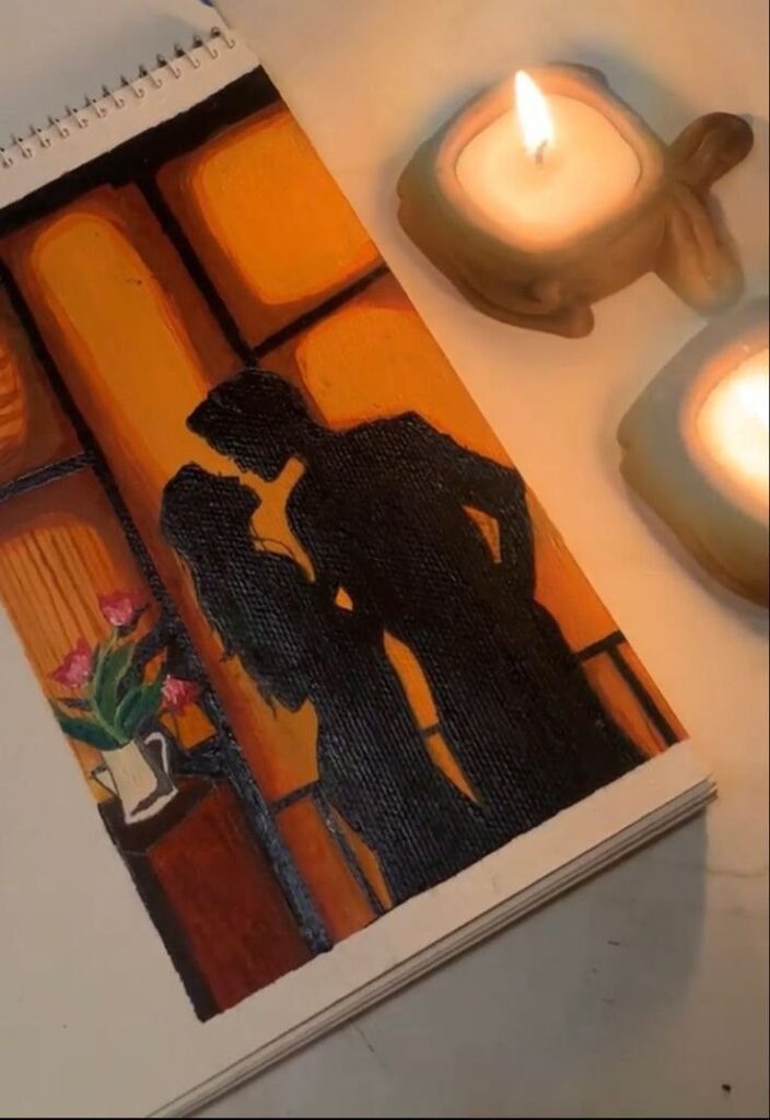 Romantic silhouette painting beside lit candles on a table, with a vase of flowers enhancing cozy ambiance.