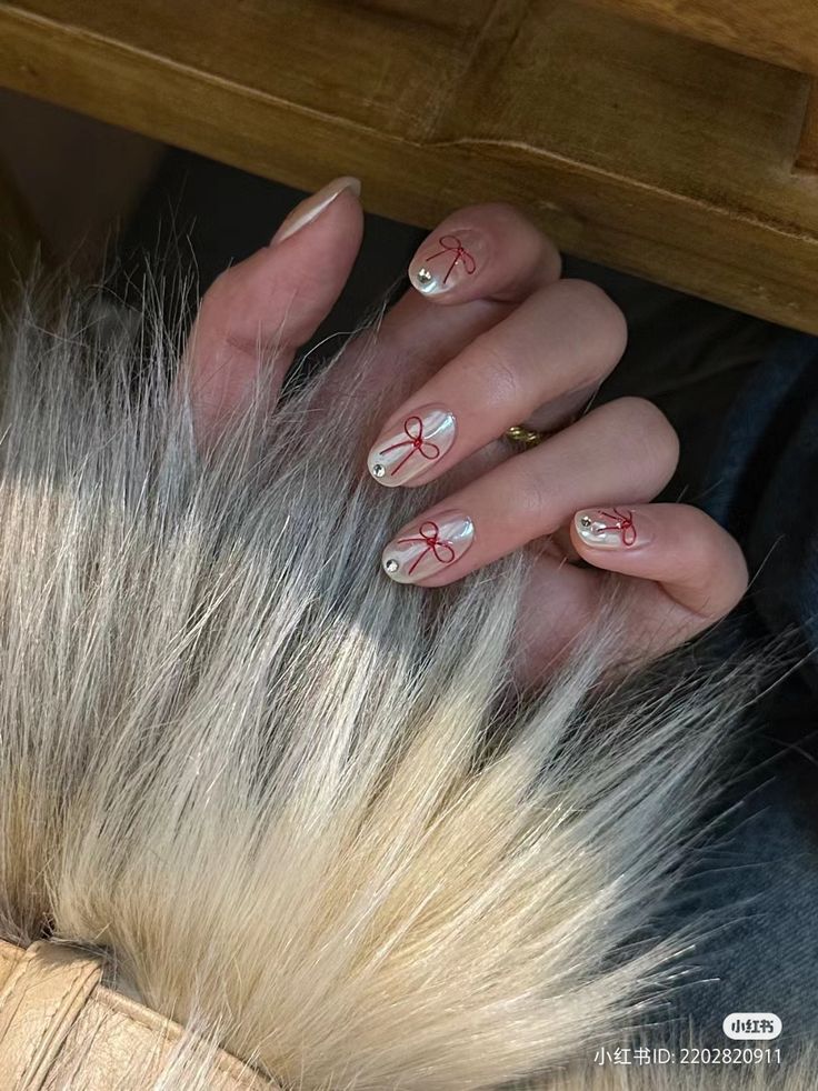 Close-up of hand with metallic nail art featuring red ribbon designs, resting on a furry surface. Luxurious manicure style.