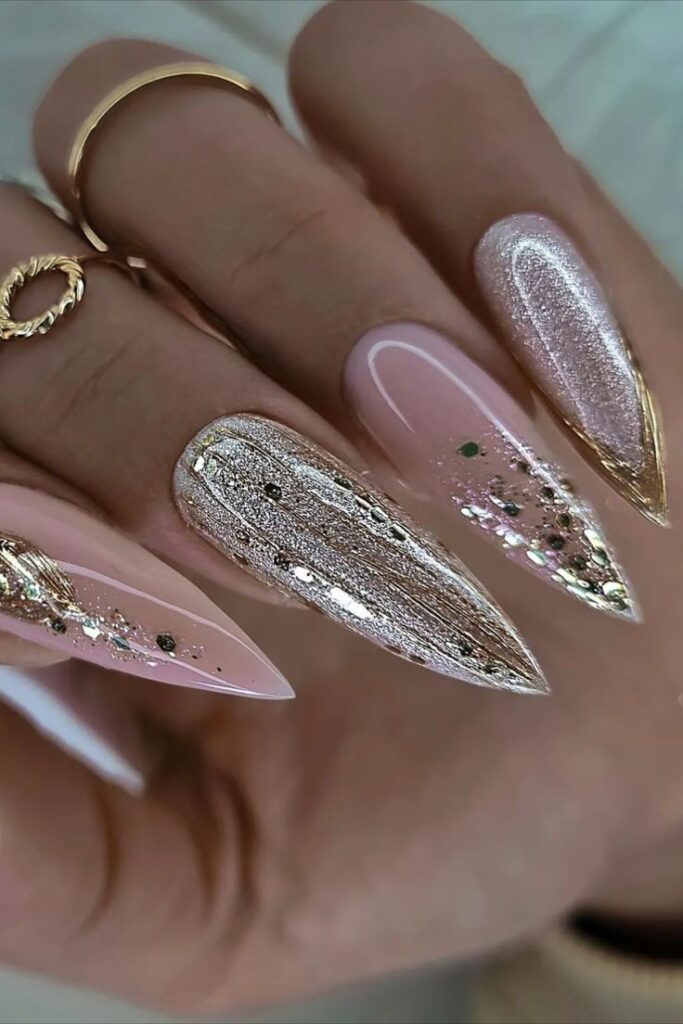 Glittery pink and gold stiletto nails with elegant rings, showcasing a chic manicure style.