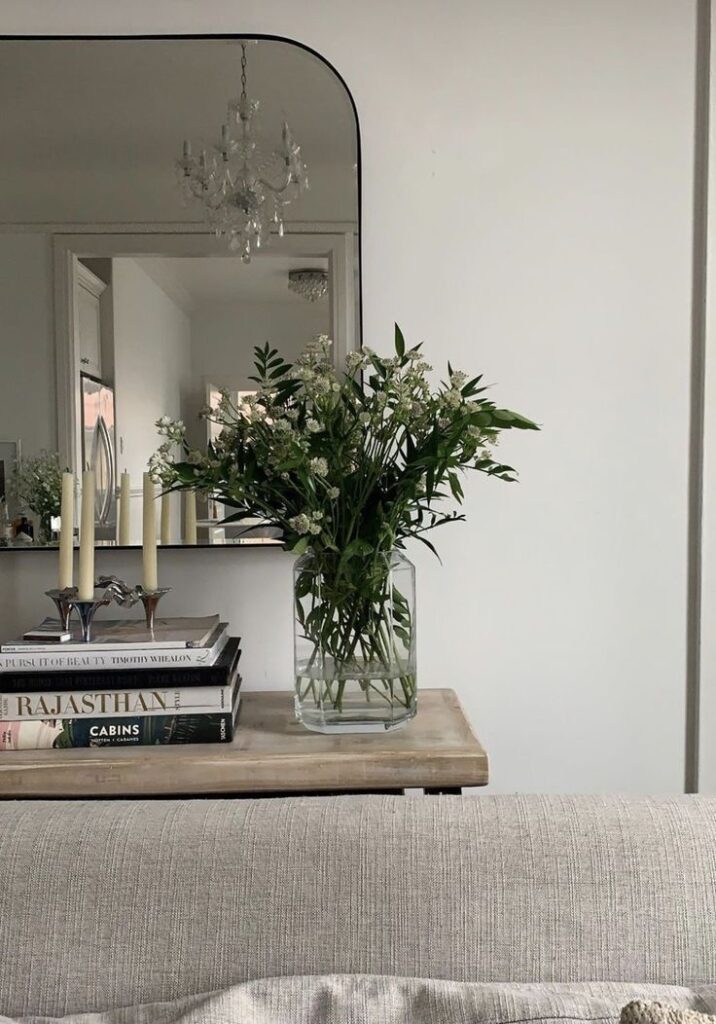 Elegant living room decor with flowers, books, and candles by a mirror on a wooden table.