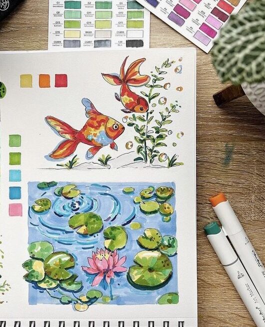 Sketchbook open to watercolor paintings of goldfish and a pond with lilies. Art markers and color swatches nearby.