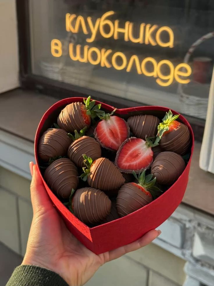 Heart-shaped box with chocolate-covered strawberries near a Клубника в шоколаде sign.