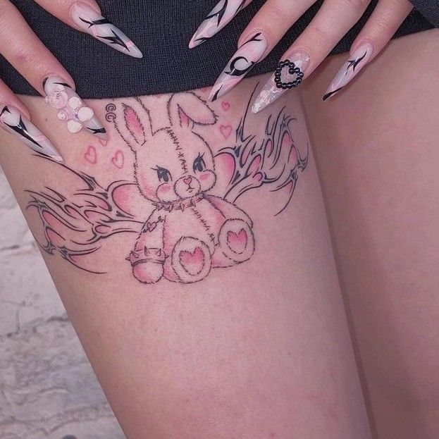 Cute stitched bunny tattoo with hearts and wings on thigh, paired with artistic nail designs.