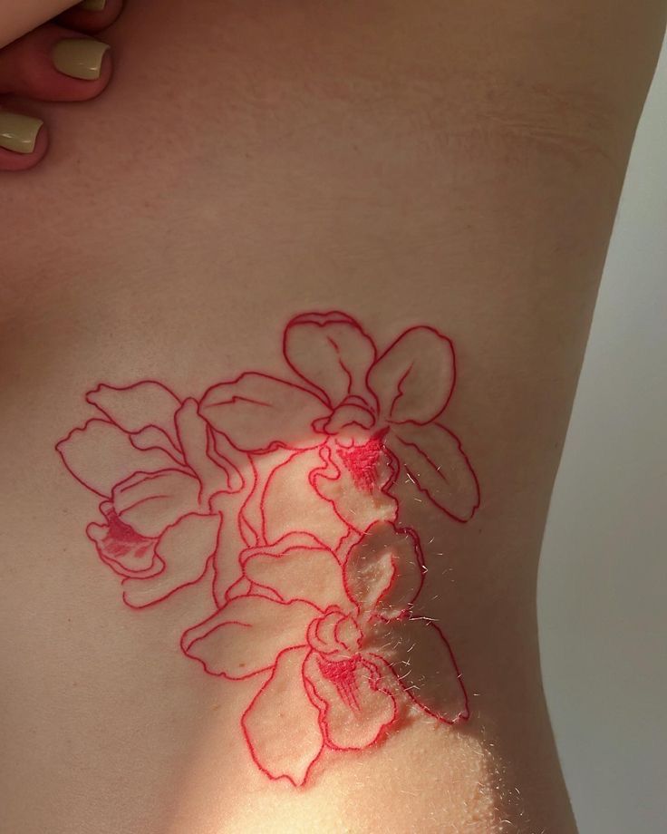 Delicate red line flower tattoo on side torso, highlighting intricate floral design against light skin.