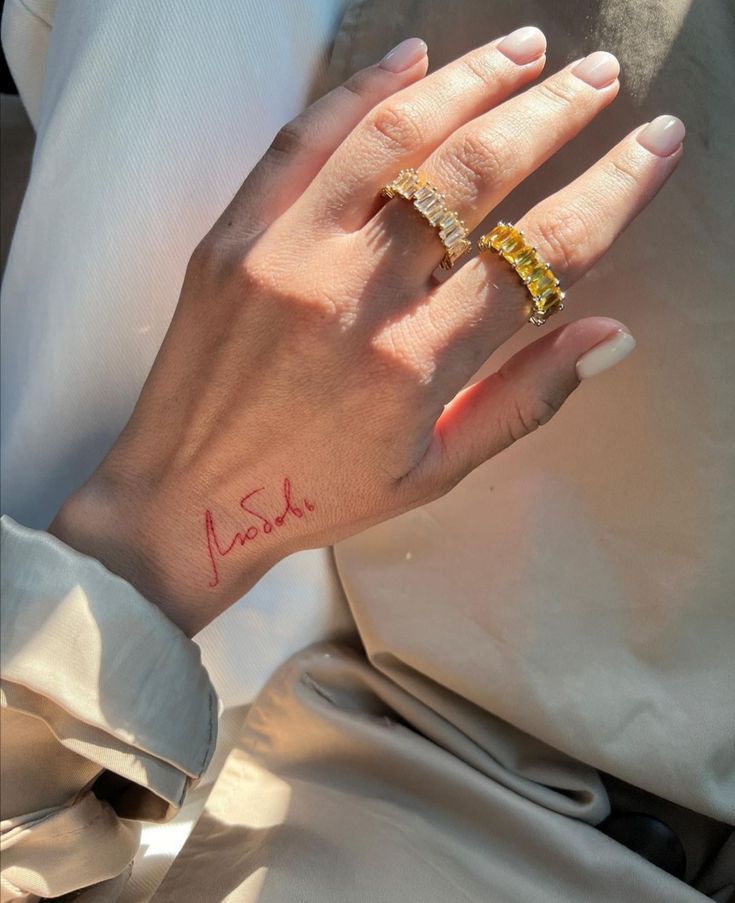 Close-up of a hand with rings and a red tattoo on the wrist, showcasing stylish jewelry and fashion accessories.