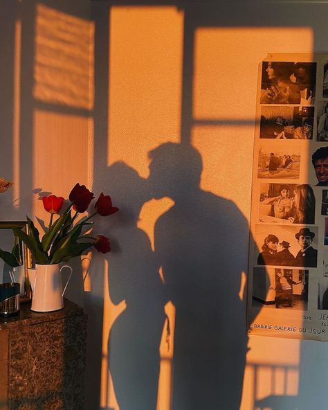 Shadow of couple kissing with flowers and photos on the wall, in warm sunset light. Romantic indoor setting.