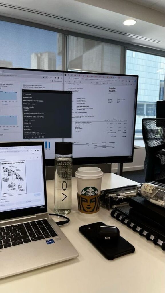 Workstation with laptop, dual monitors, water bottle, coffee cup, phone, and stationery in a modern office environment.