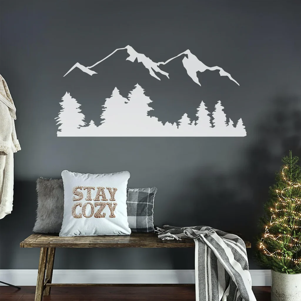 Cozy living room with mountain wall art, Stay Cozy pillow, and small lit Christmas tree on bench.