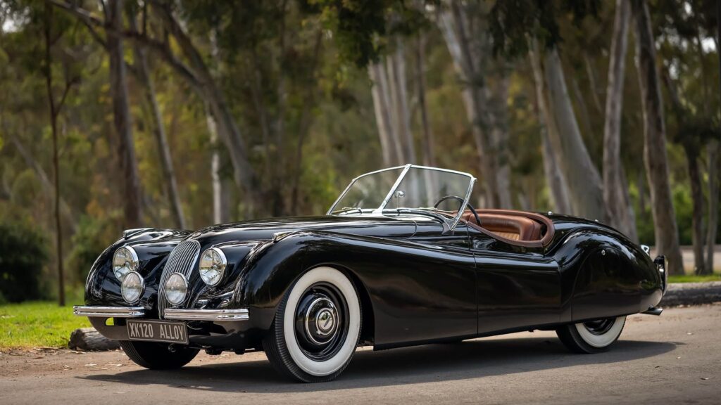 Classic black convertible car parked in a scenic wooded area.