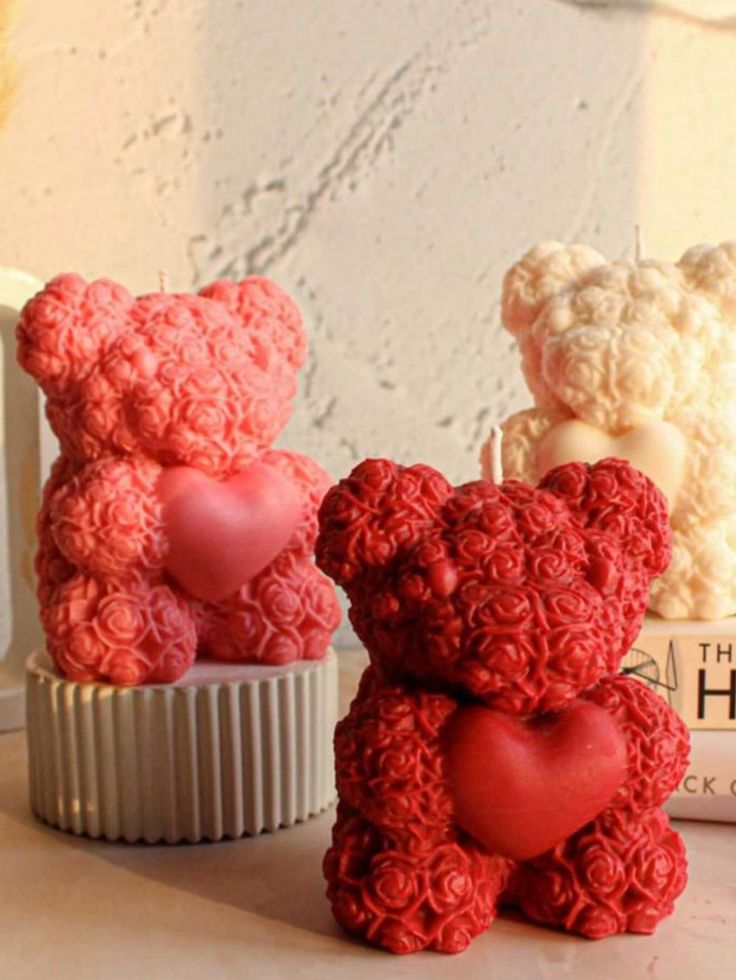 Three rose-patterned bear candles with heart shapes, featuring red and pink colors, placed against a textured background.