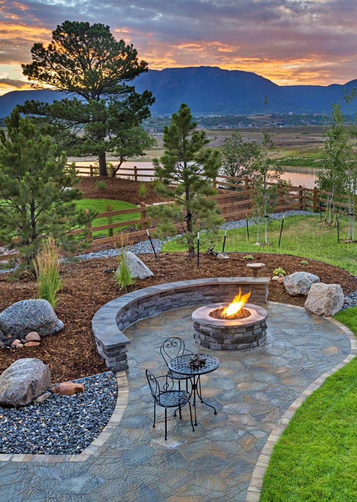 Backyard patio with fire pit, seating, and mountain view at sunset, surrounded by trees and a peaceful garden setting.