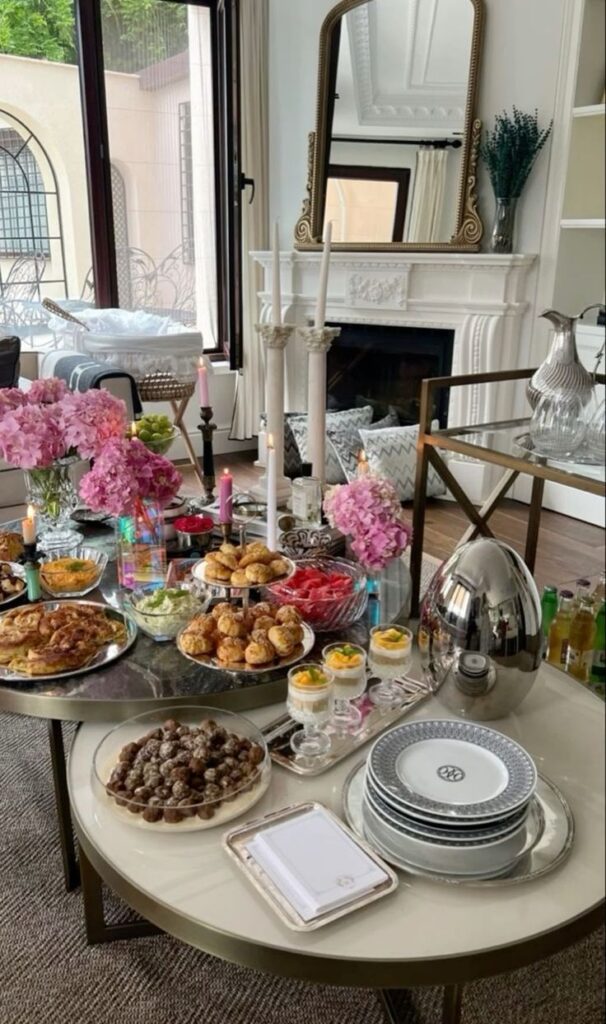 Elegant brunch setup with pastries, flowers, and candles in a cozy living room with a fireplace and mirror.