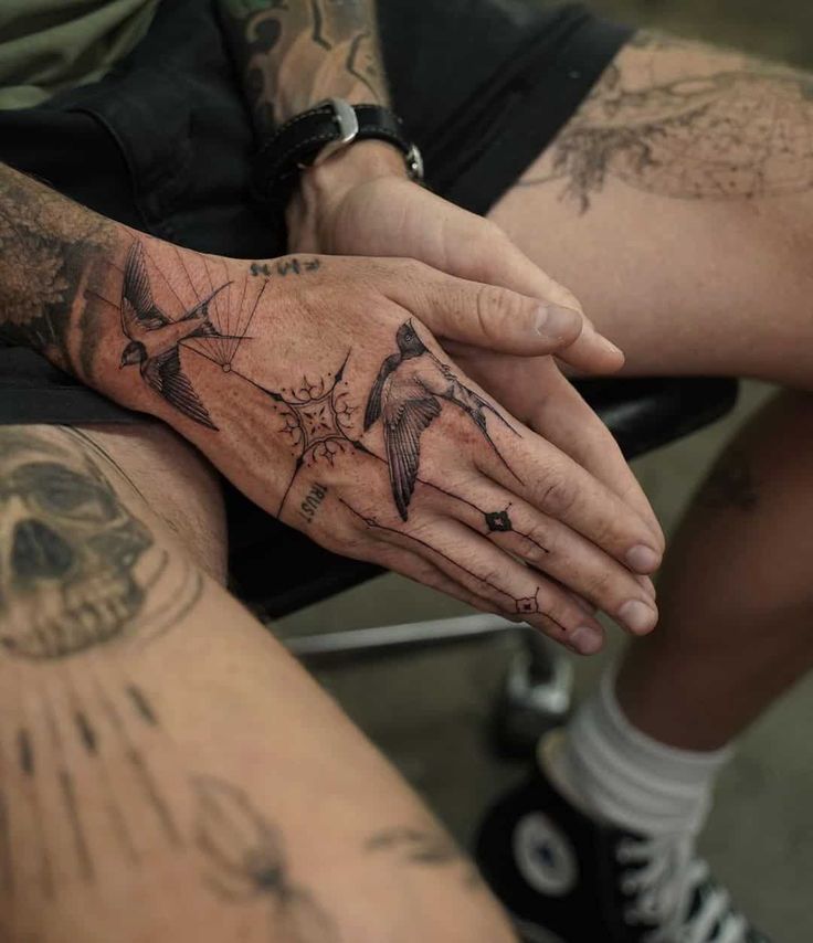 Man sitting with detailed bird tattoos on hand, showcasing artistic body art in a relaxed setting.