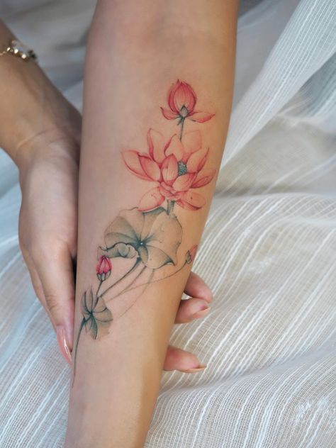 Delicate lotus flower tattoo on forearm, blending pink and green hues, symbolizing beauty and purity.