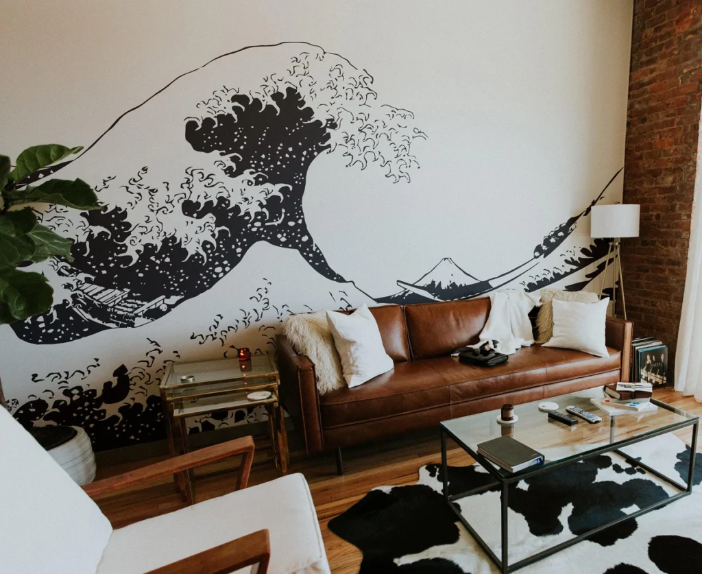 Living room with wave mural, brown leather sofa, modern decor, and glass coffee table on black and white rug.