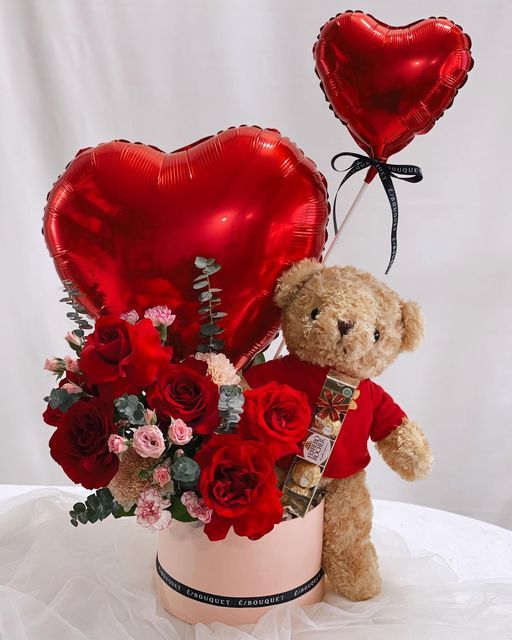 Teddy bear with roses, chocolates, and heart balloons in a gift arrangement, perfect for Valentine's Day.