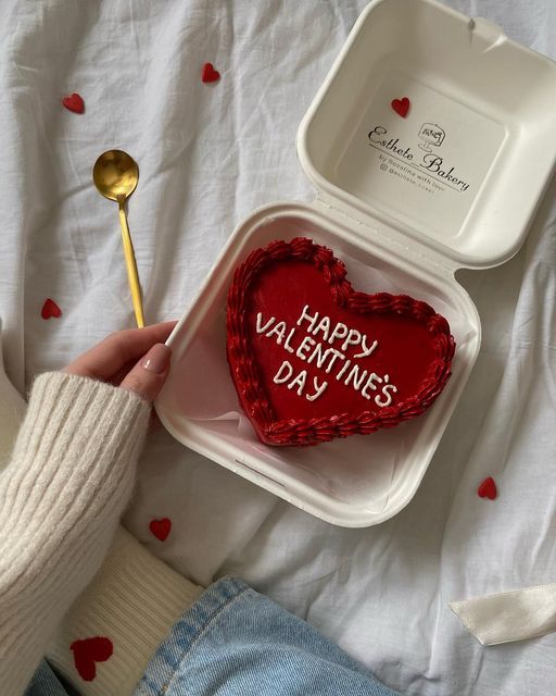 Heart-shaped Valentine's Day cake in a box with a gold spoon and cozy setting.