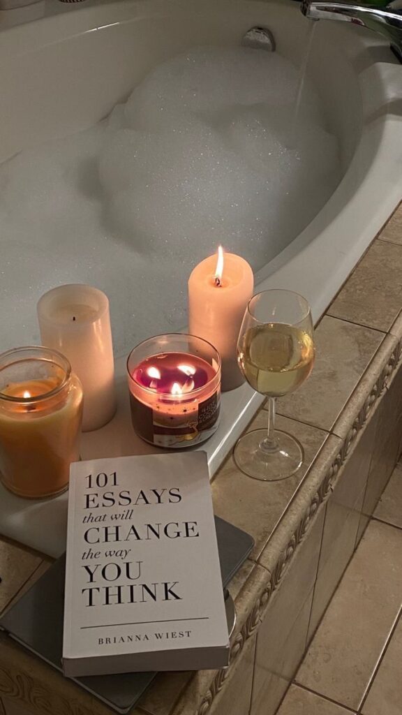 Cozy bath setting with candles, book, and wine glass on a tub for a relaxing reading experience.