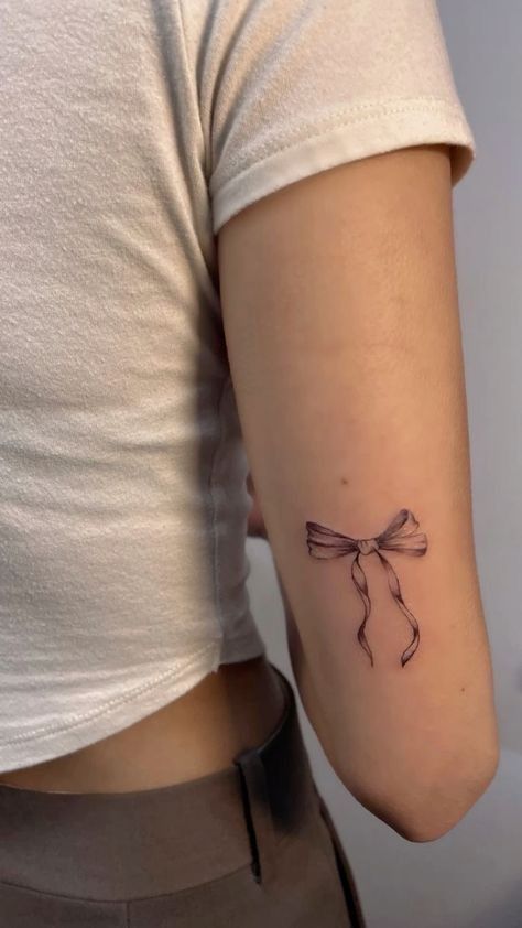 Minimalist ribbon tattoo on a person's arm, wearing a white shirt and gray pants.