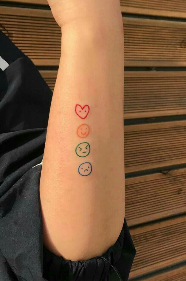 Tattoo of four colorful emoticons on forearm: red heart, orange smile, green frown, blue sad face.