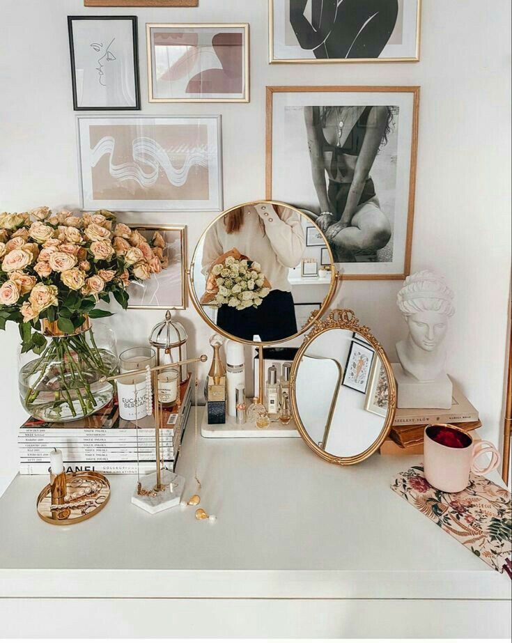 Stylish vanity with gold accents, mirrors, and a bouquet of roses, surrounded by framed art and a sculpted bust.