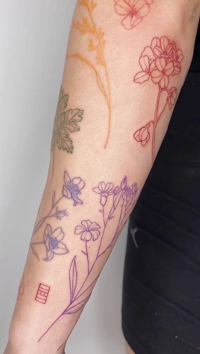 Arm with colorful floral tattoos featuring delicate outlined flowers and leaves in various ink shades.