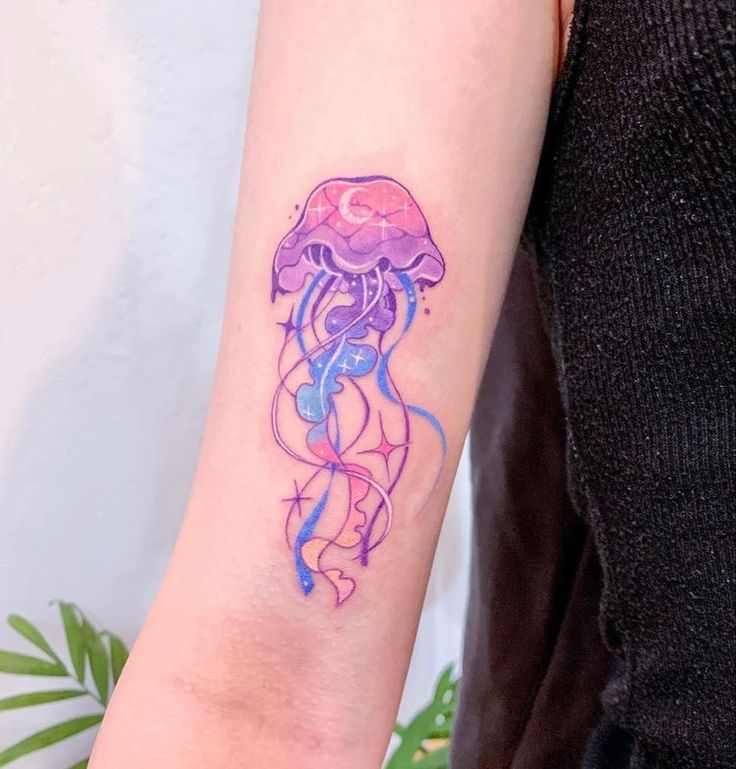 Colorful jellyfish tattoo with cosmic design on person's arm, featuring purple and blue hues with star accents.