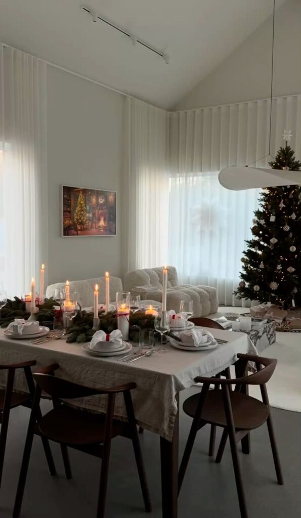 Festive dining room with elegant table setting, candles, and Christmas tree creating a cozy holiday ambiance.