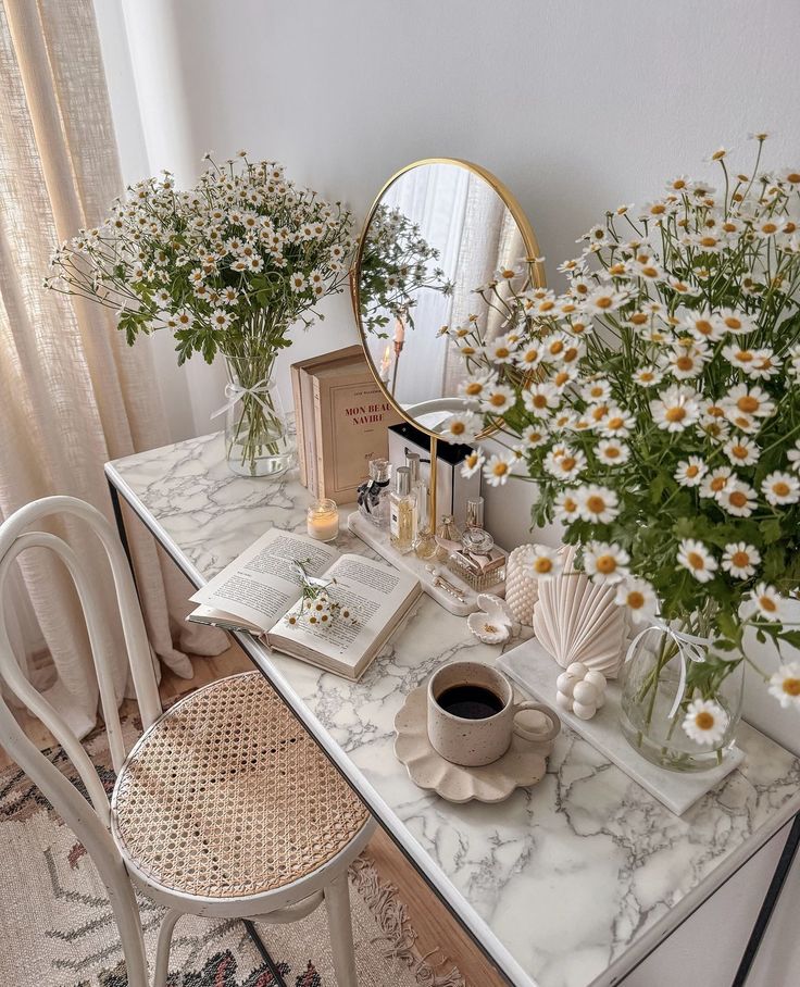 Cozy vanity with flowers, open book, coffee, and mirror on marble top. Serene and stylish home decor setup.