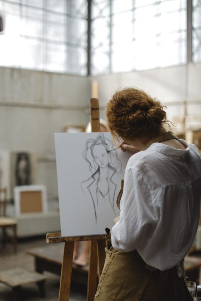 Artist sketching a woman's portrait on canvas in a bright studio.