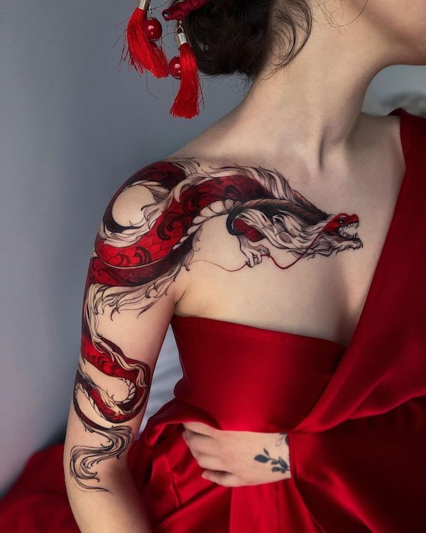 Red dragon tattoo on woman's shoulder and arm, complementing her red dress and accessories.