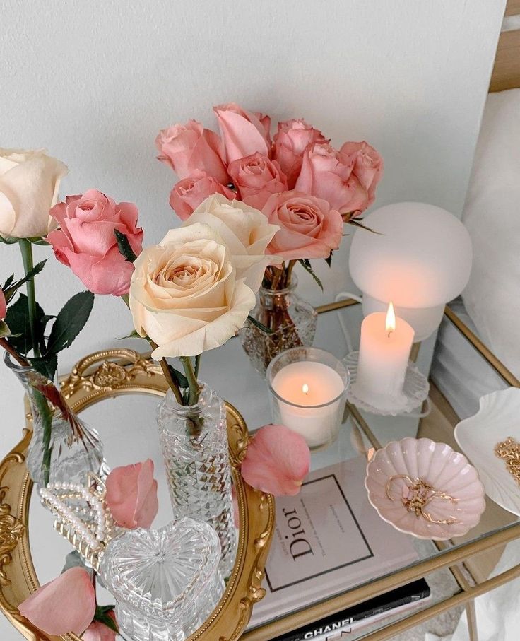 Elegant table with pink roses, candles, and decor on gold mirror tray for a cozy, chic ambiance.