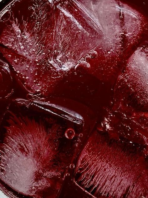 Close-up of red liquid with ice cubes, showing texture and bubbles for a refreshing drink concept.