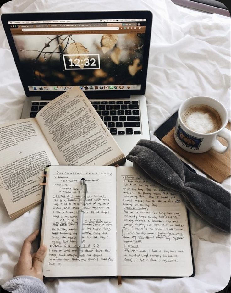 Cozy workspace with a laptop, open journals, a book, and a hot cup of coffee on a bed.