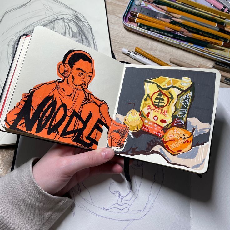 Artistic sketchbook open to colorful drawings of a person and snack items, surrounded by art supplies on a desk.